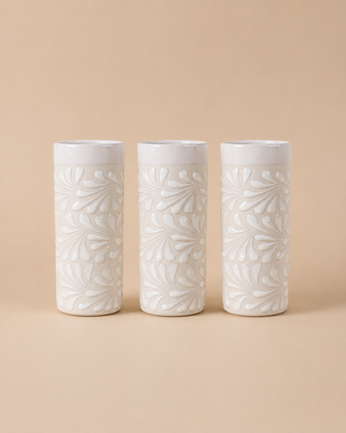Three white ceramic tumblers with leaf patterns on a beige background