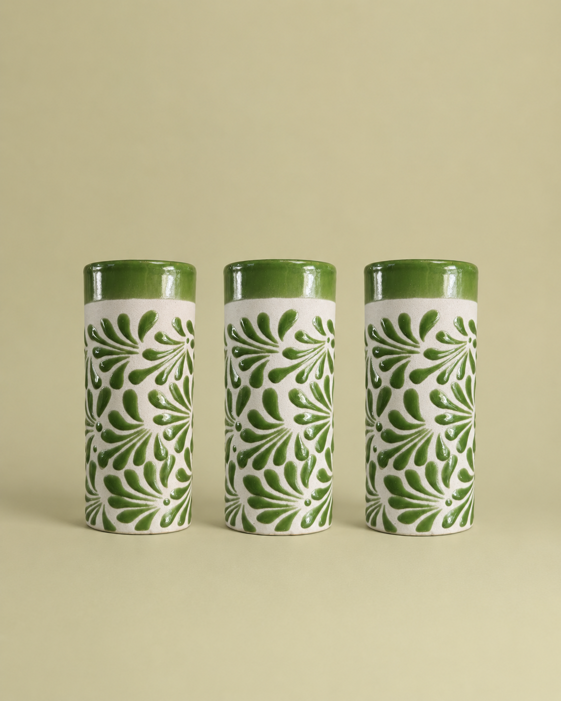 Three cylindrical ceramic cups with green and white patterns on a beige background