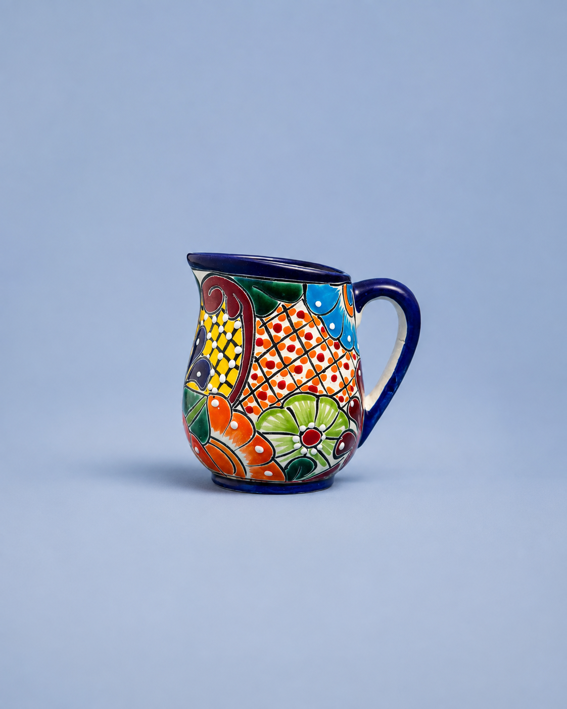 A small ceramic pitcher with a colorful hand-painted pattern and a dark blue handle and rim, set against a solid light blue background.