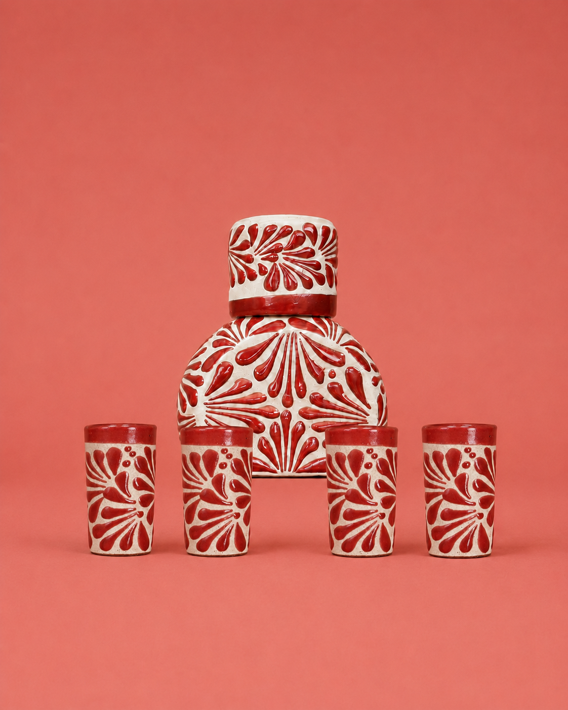Ceramic set with a central jar and four matching cups on a red background