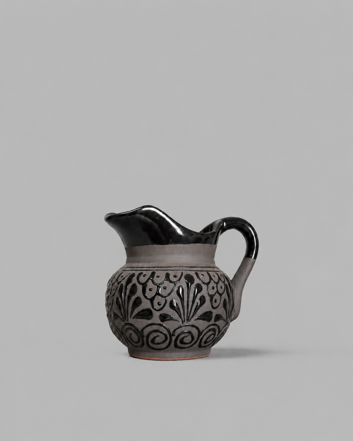 Ceramic pitcher with black floral patterns on a gray background