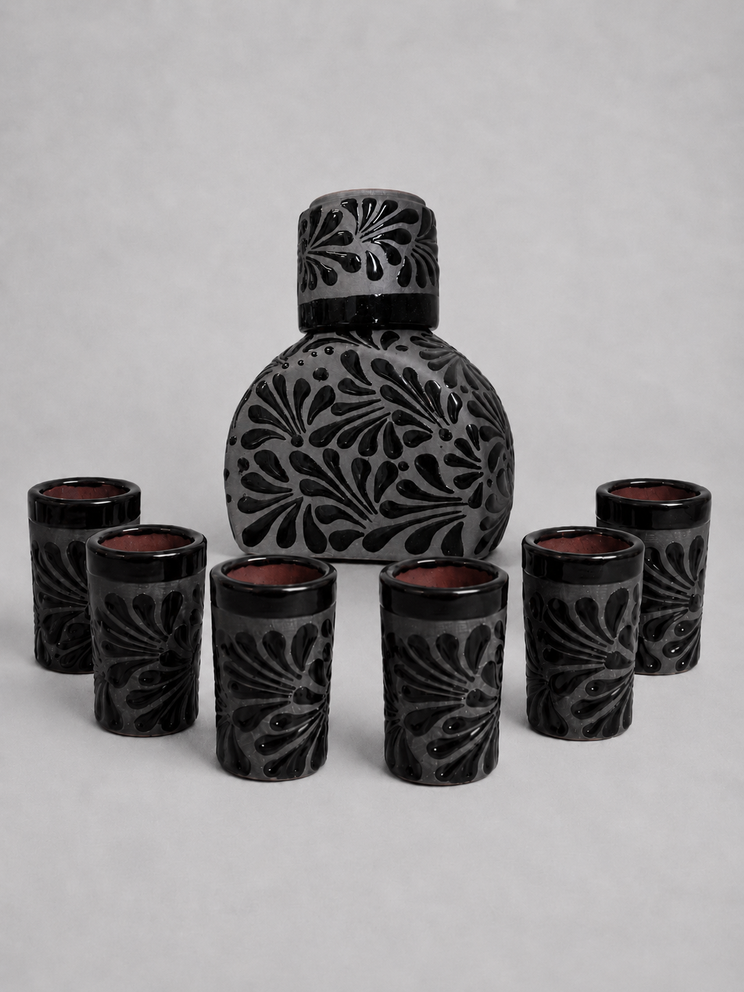 Black ceramic tequila bottle set with intricate designs on a gray background