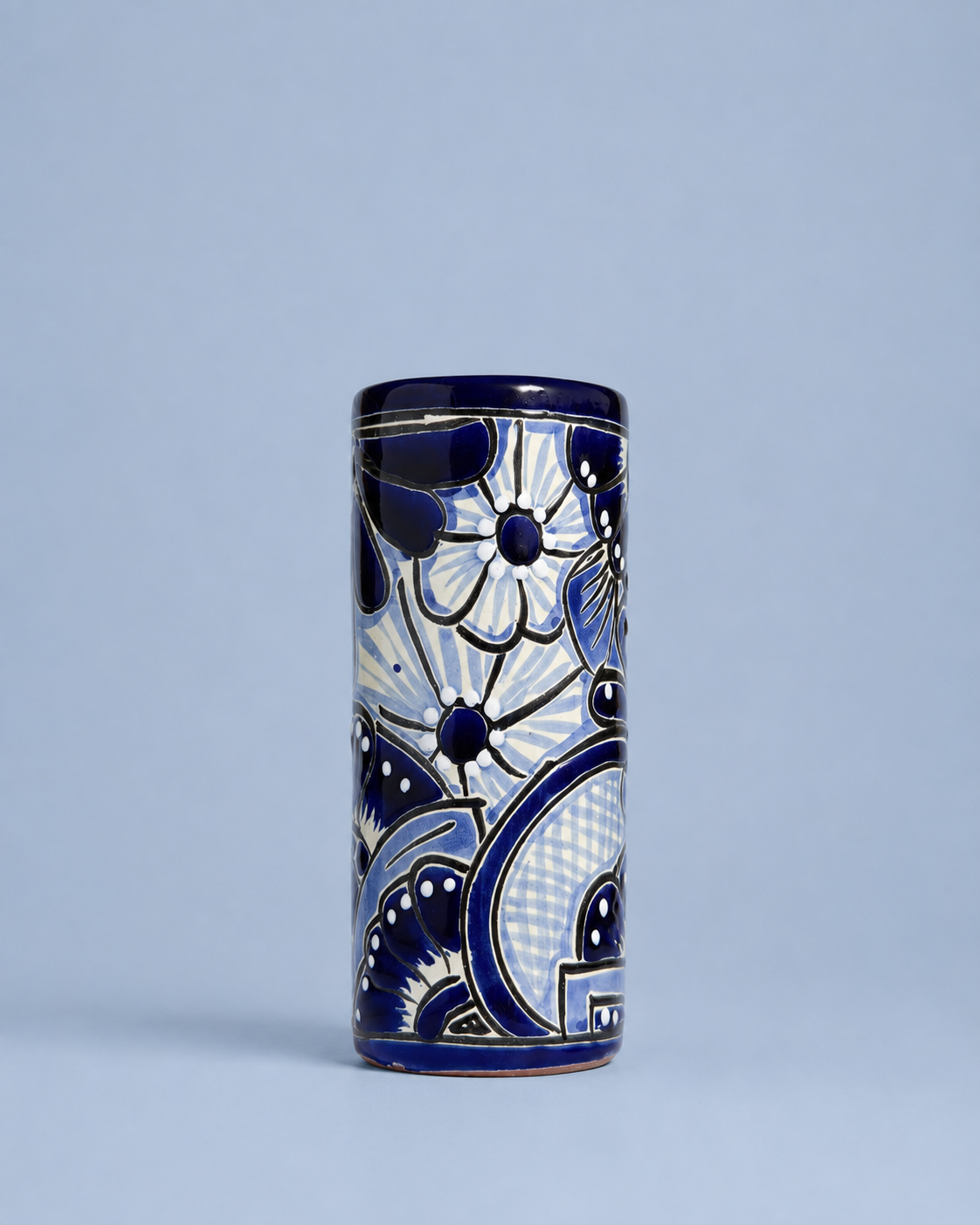 A tall cylindrical ceramic vase with a cobalt blue and white hand-painted floral and geometric pattern, set against a solid light blue-gray background.