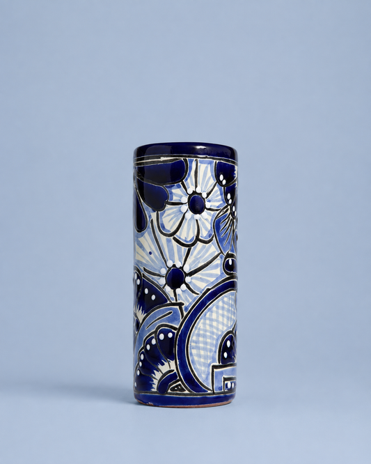 A tall cylindrical ceramic vase with a cobalt blue and white hand-painted floral and geometric pattern, set against a solid light blue-gray background.