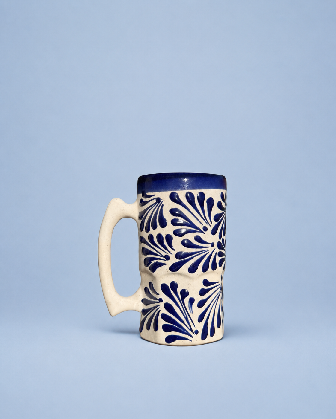 A ceramic mug with a cream-colored body, a dark blue handle, and a dark blue floral pattern on a light blue background.
