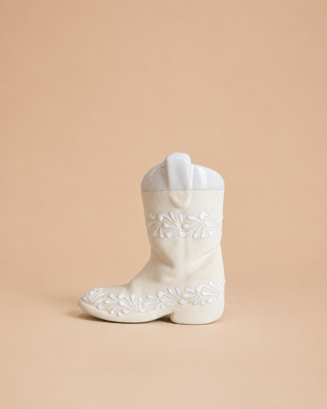 White ceramic boot with floral embroidery on a beige background