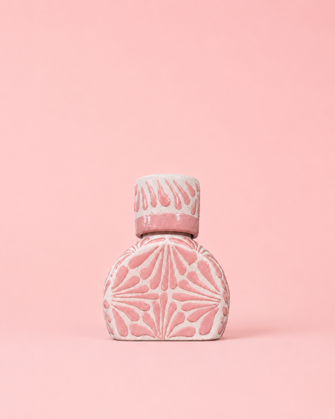 Pink ceramic liquor bottle with decorative design on a pink background