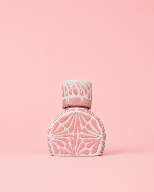 Pink ceramic liquor bottle with decorative design on a pink background