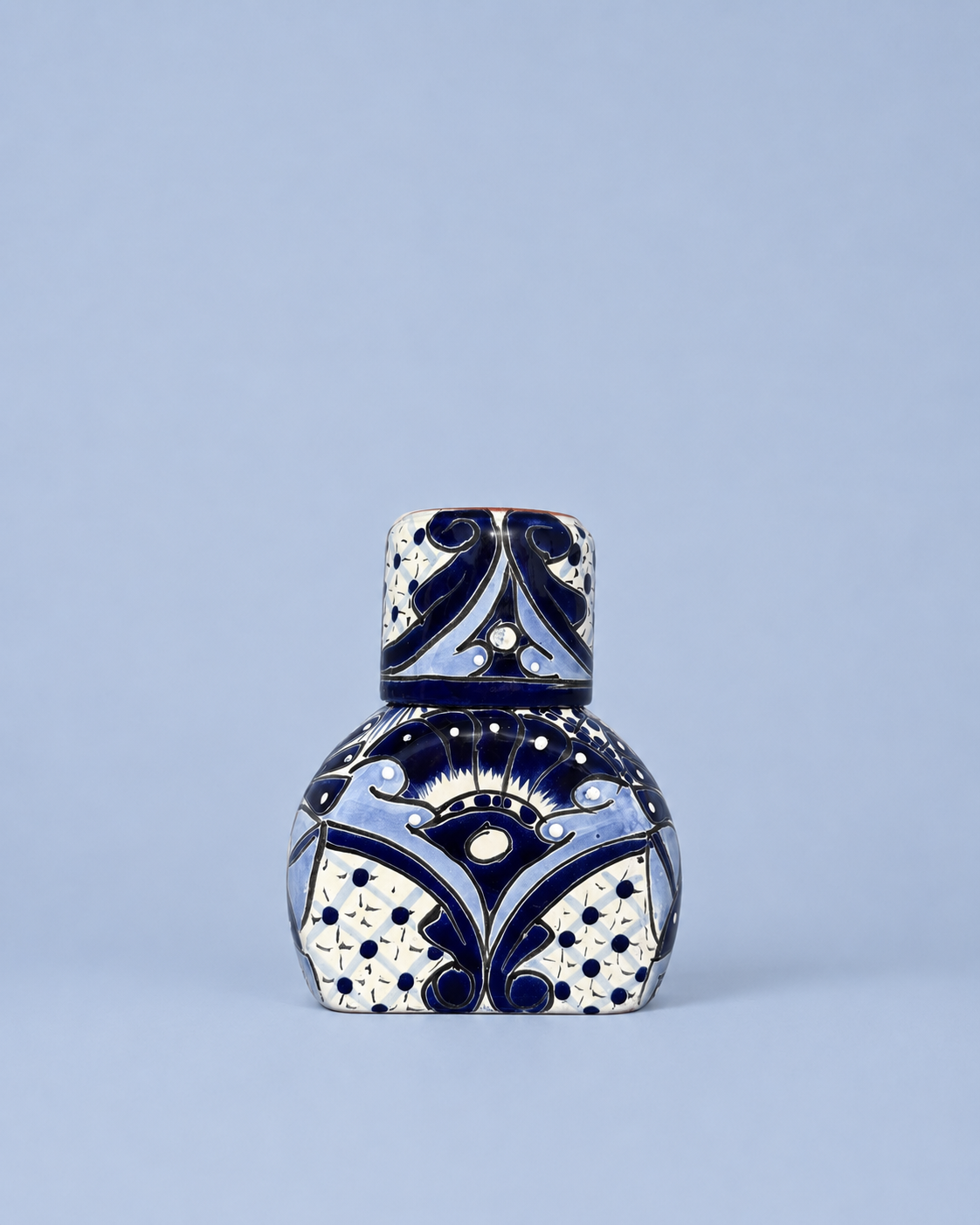 A small decorative ceramic bottle with a matching lid, decorated with a blue and white geometric pattern, set against a solid light blue background.