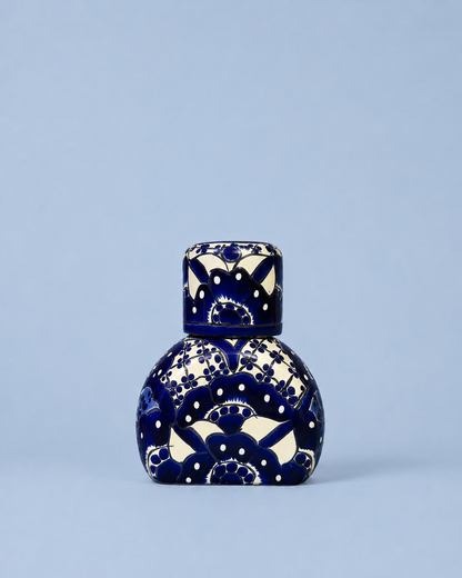 A small decorative ceramic bottle with a matching lid, featuring a deep cobalt blue and cream floral pattern, set against a solid light blue background.