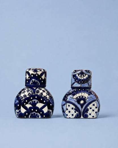 Two small decorative ceramic bottles with matching lids, decorated with intricate blue and white hand-painted patterns, set against a solid light blue background.