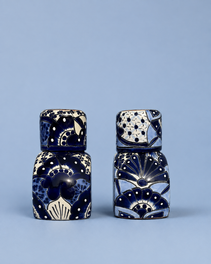 Two small decorative ceramic containers with matching lids, decorated with navy blue and cream floral and geometric patterns, set against a solid light blue background.