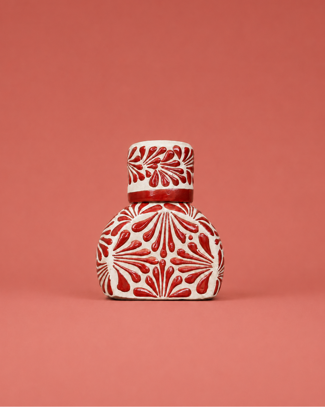 Decorative ceramic liquor bottle with red patterns on a coral background