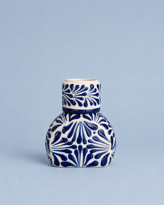 A small ceramic bottle or vase with a rounded body and narrow neck, decorated with a bold blue and white floral pattern, set against a solid light blue background.