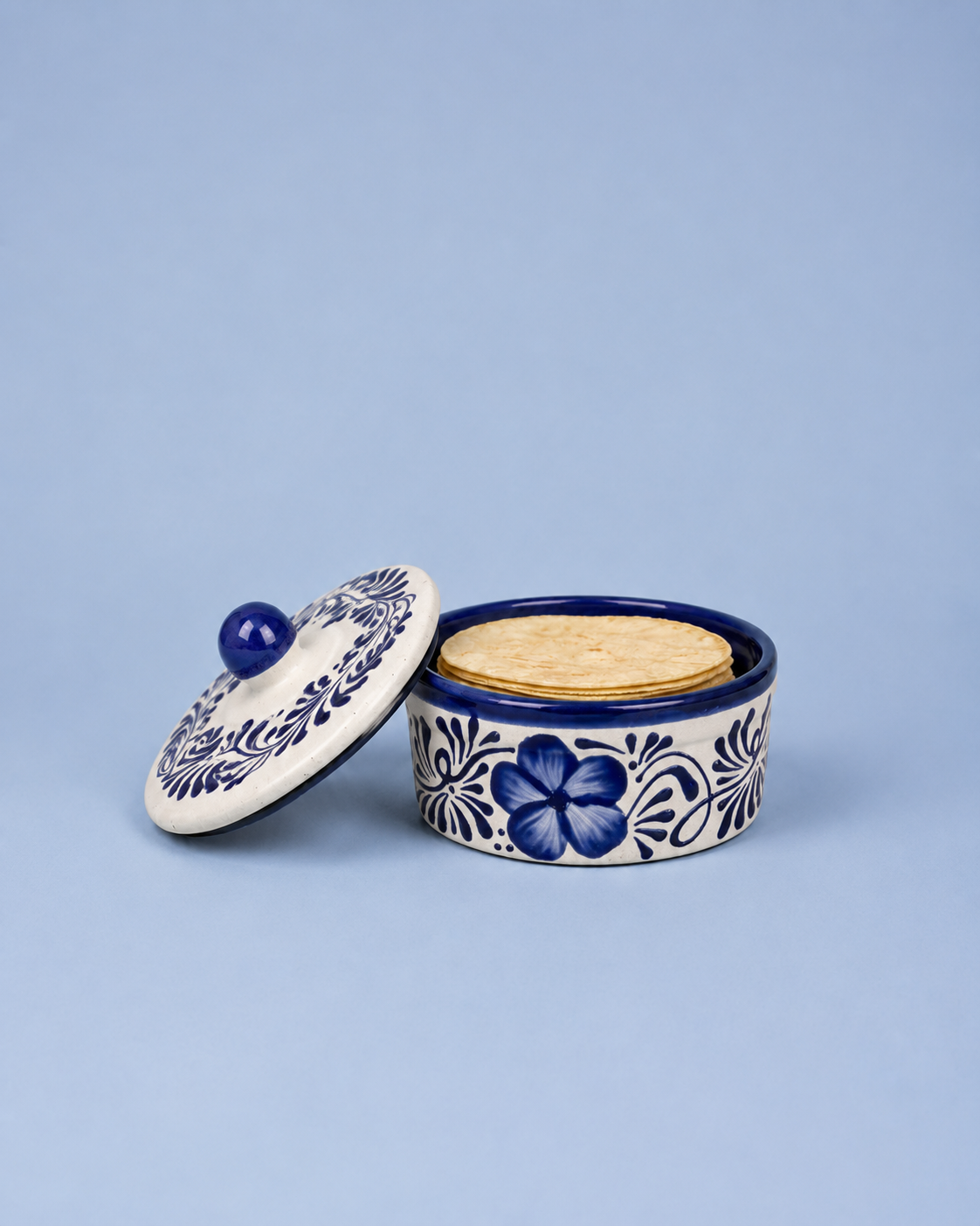 A small round ceramic lidded container with a blue floral pattern on a white base, shown open with a cork stopper on a light blue background.