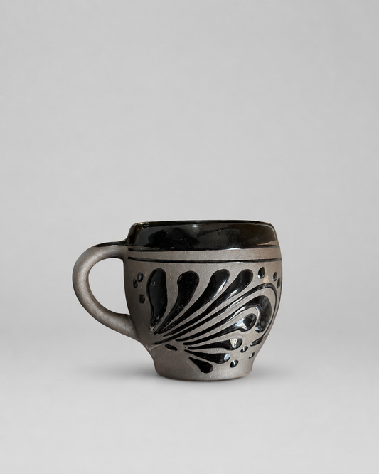 Black ceramic mug with decorative patterns on a light gray background