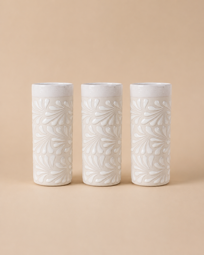 Three white ceramic tumblers with leaf patterns on a beige background