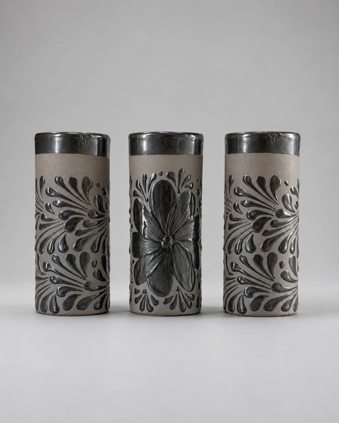 Three cylindrical ceramic cups with floral patterns on a gray background