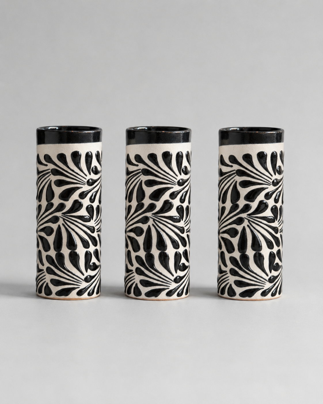 Three cylindrical ceramic cups with black and white pattern on a gray background
