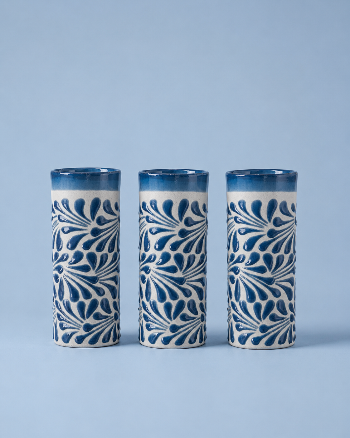 Three ceramic tumblers with blue and white pattern on a light blue background