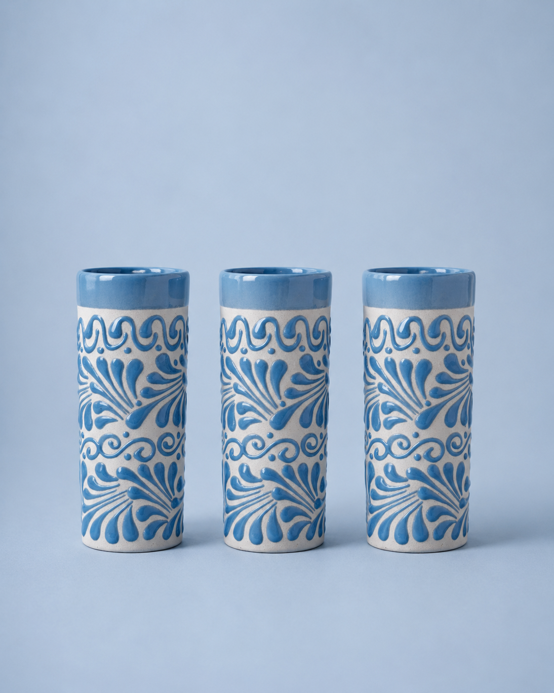 Three ceramic tumblers with blue floral patterns on a light blue background