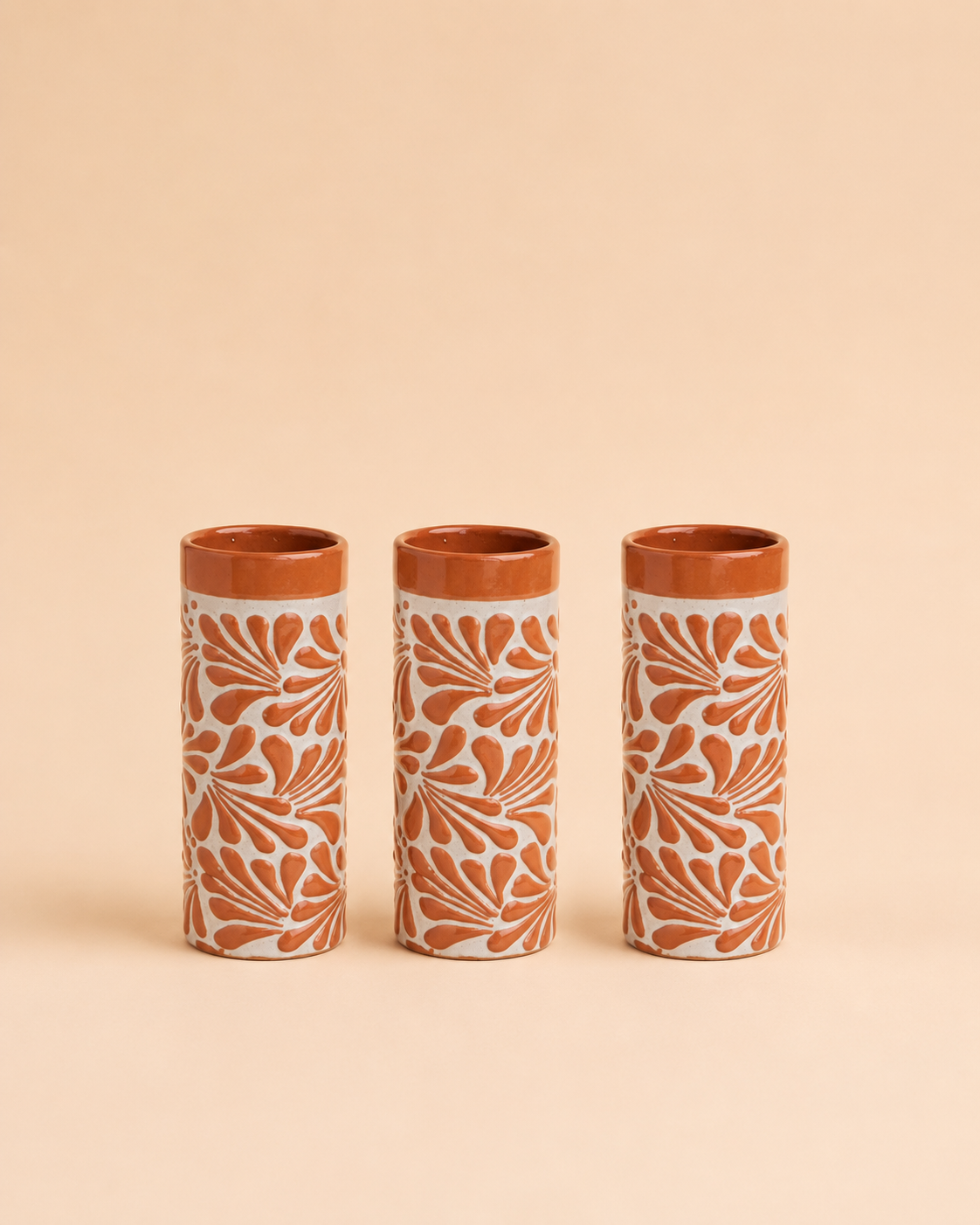 Three cylindrical ceramic cups with floral patterns on a beige background