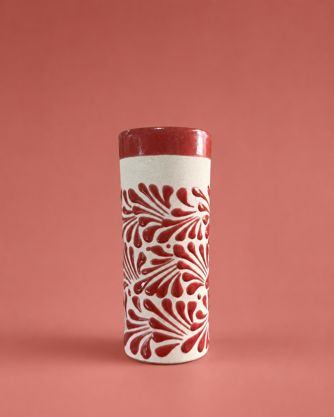 Tall cylindrical cup with red and white pattern on a pink background