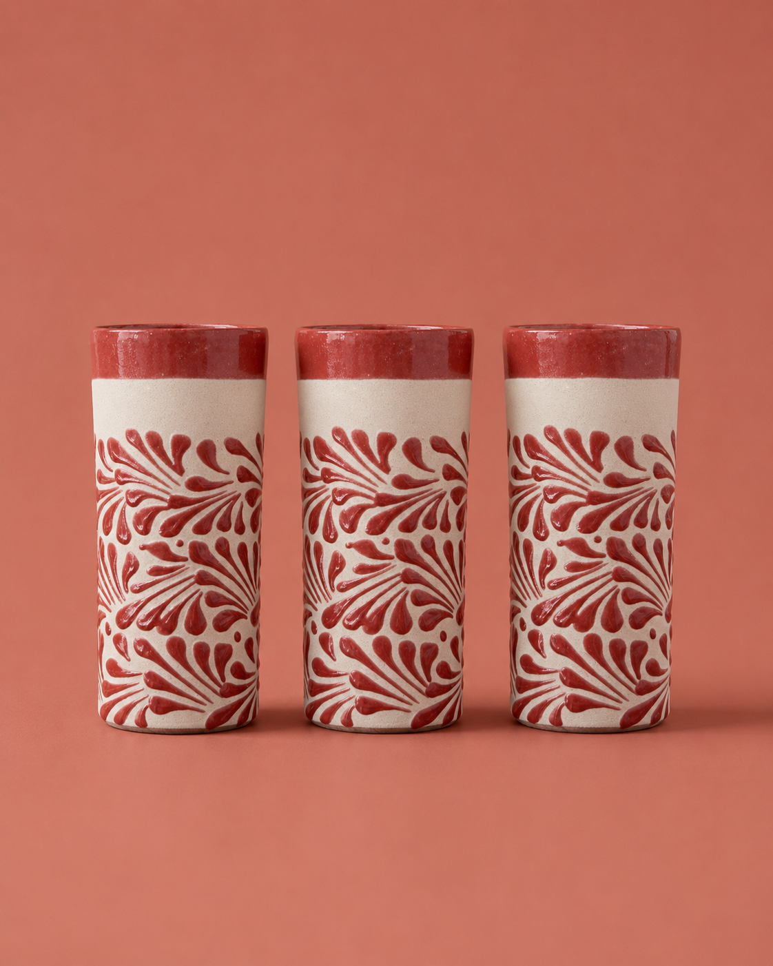 Three cylindrical ceramic containers with red floral patterns on a red background