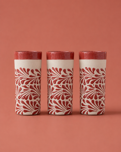 Three cylindrical ceramic containers with red floral patterns on a red background