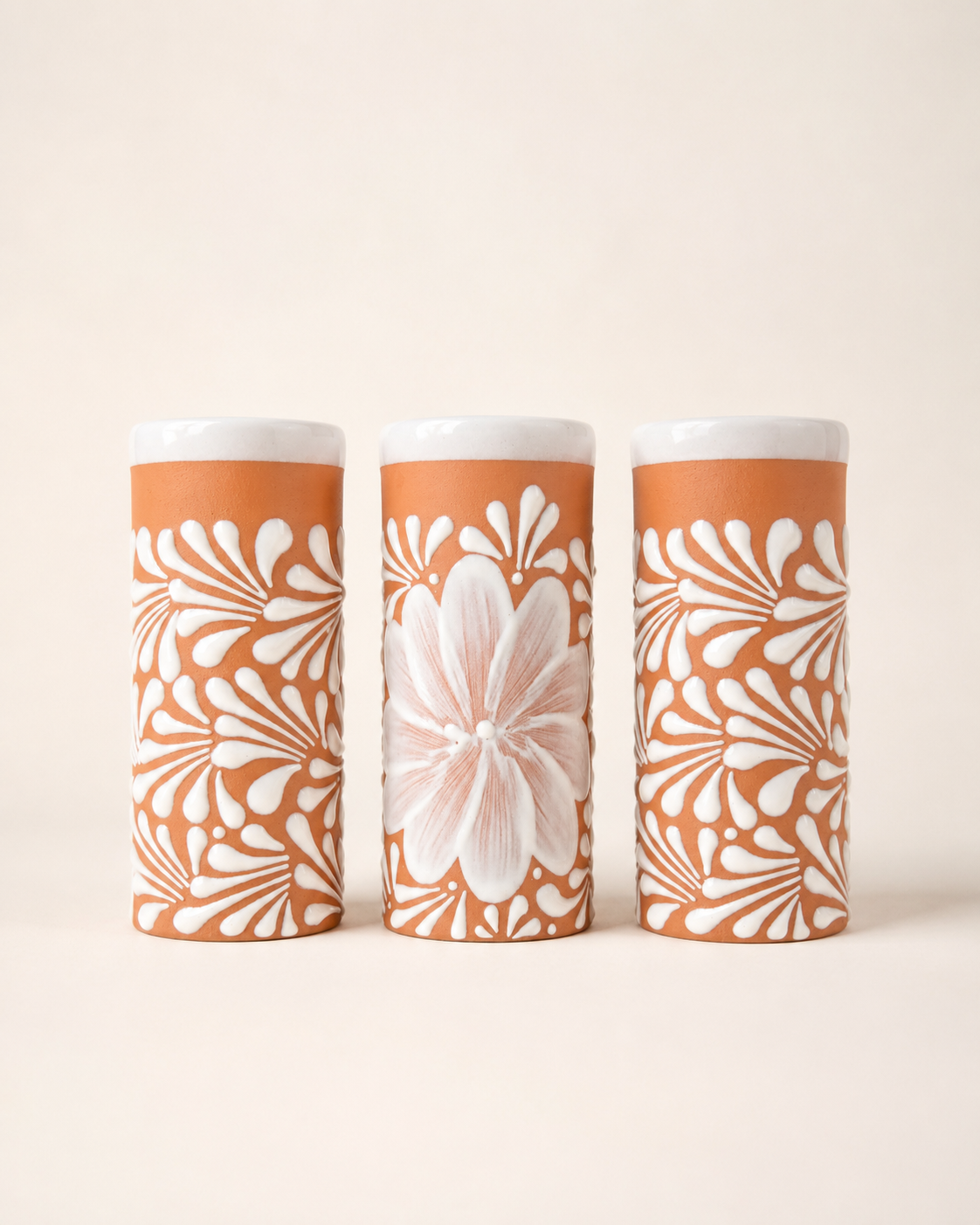 Three cylindrical cups with floral patterns on a beige background