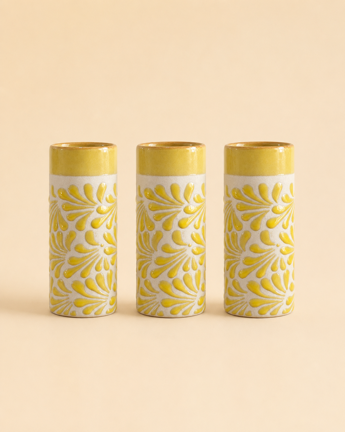 Three cylindrical cups with yellow floral patterns on a beige background