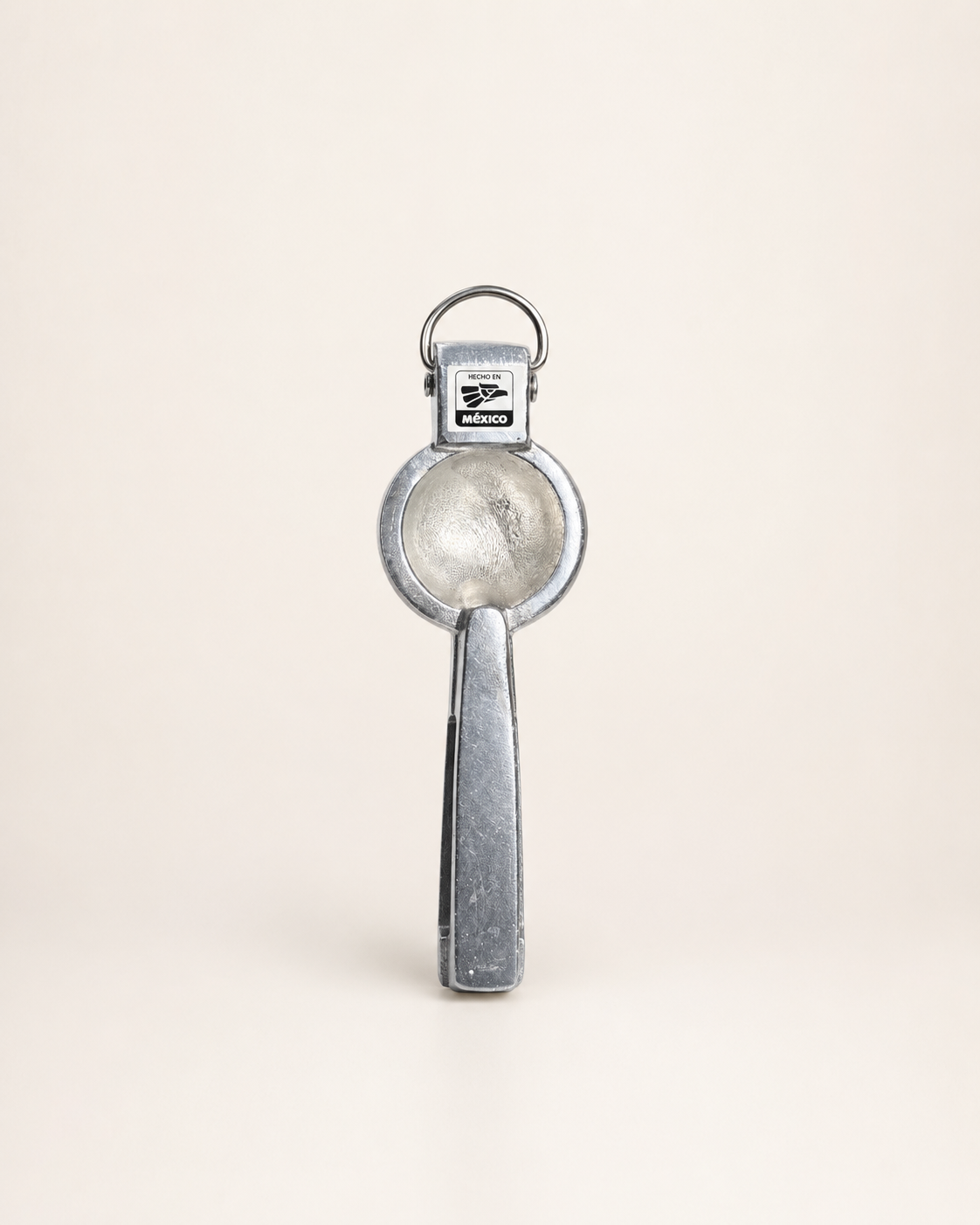 A vintage silver metal key ring opener with a circular blade and a rectangular handle, shown standing upright on a light beige background.