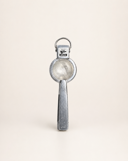 A vintage silver metal key ring opener with a circular blade and a rectangular handle, shown standing upright on a light beige background.