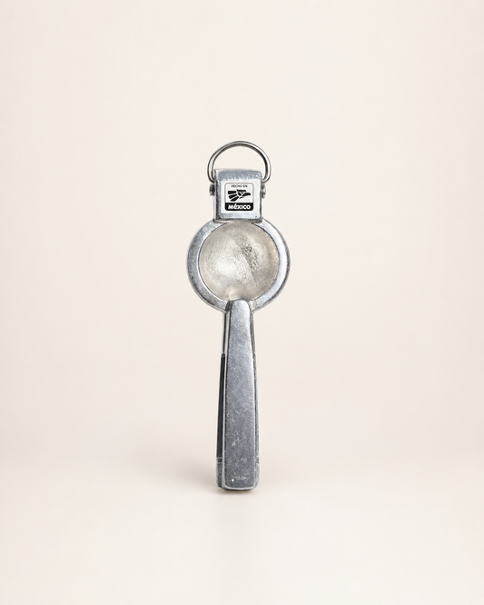 A vintage silver metal key ring opener with a circular blade and a rectangular handle, shown standing upright on a light beige background.