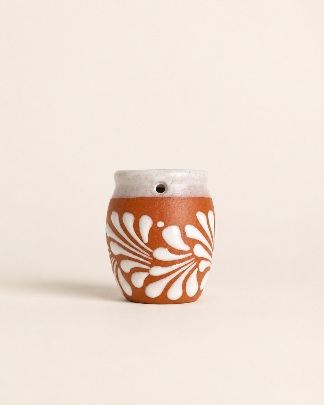 Ceramic shot glass with white floral pattern on a beige background