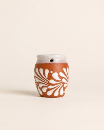 Ceramic shot glass with white floral pattern on a beige background
