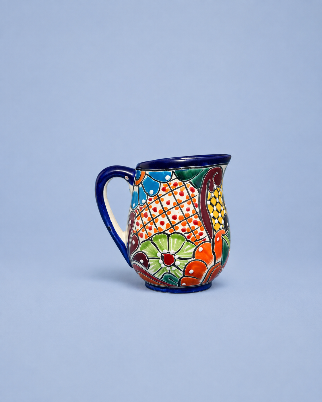 A colorful hand-painted ceramic mug with a blue handle and rim, featuring a traditional Spanish or Mexican floral and geometric pattern, set against a solid light blue background.