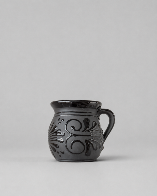 Black ceramic mug with decorative patterns on a gray background