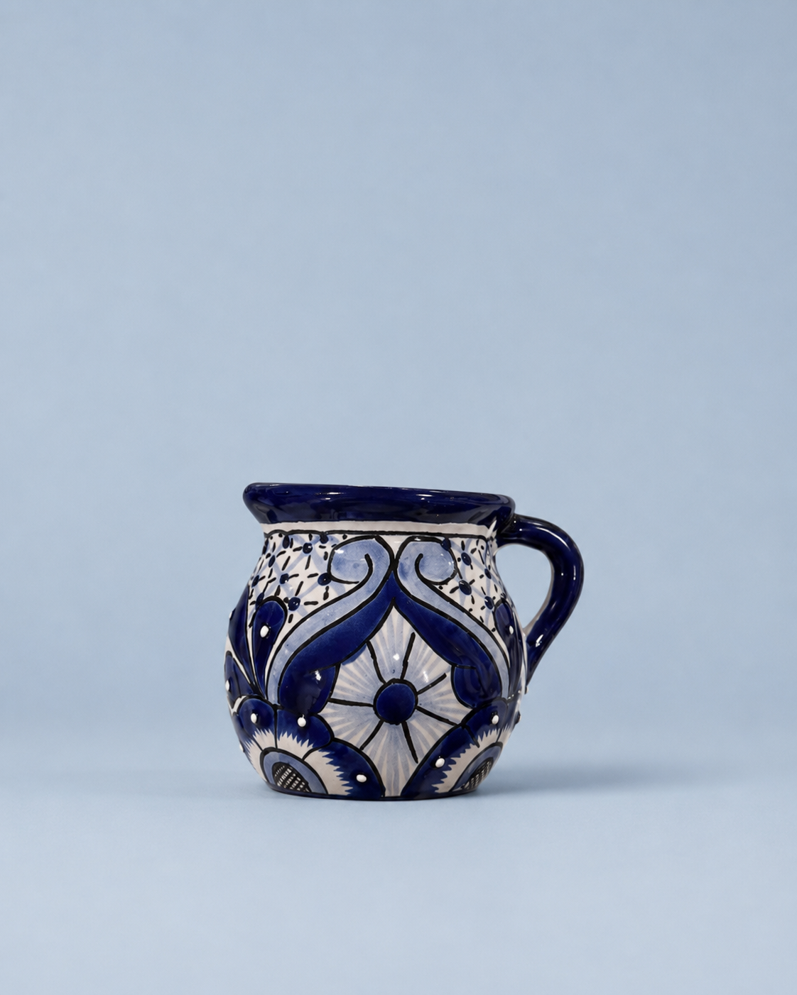 A small ceramic mug with a handle, decorated with a traditional blue and white floral pattern, set against a solid light blue background.
