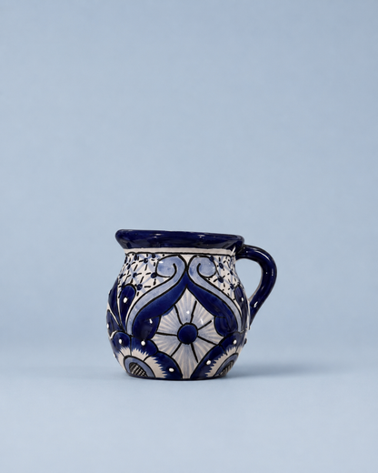 A small ceramic mug with a handle, decorated with a traditional blue and white floral pattern, set against a solid light blue background.