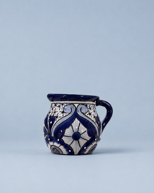A small ceramic mug with a handle, decorated with a traditional blue and white floral pattern, set against a solid light blue background.