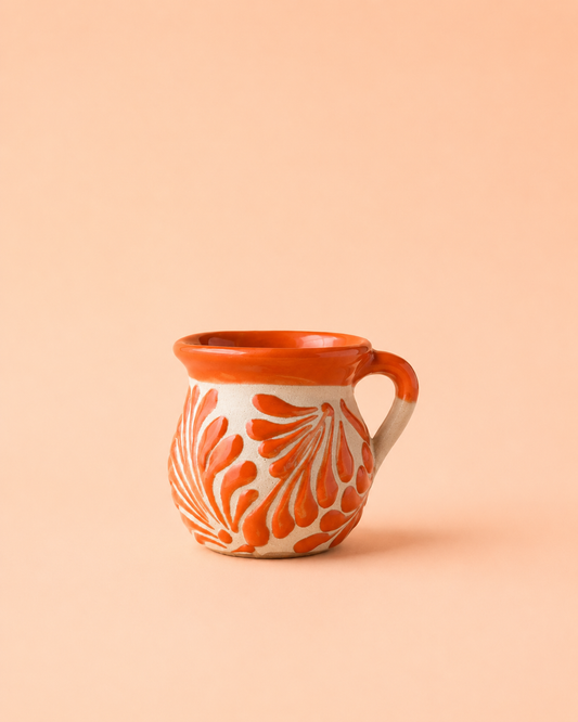 A small ceramic mug with a warm orange and white floral pattern, set against a solid peach background.