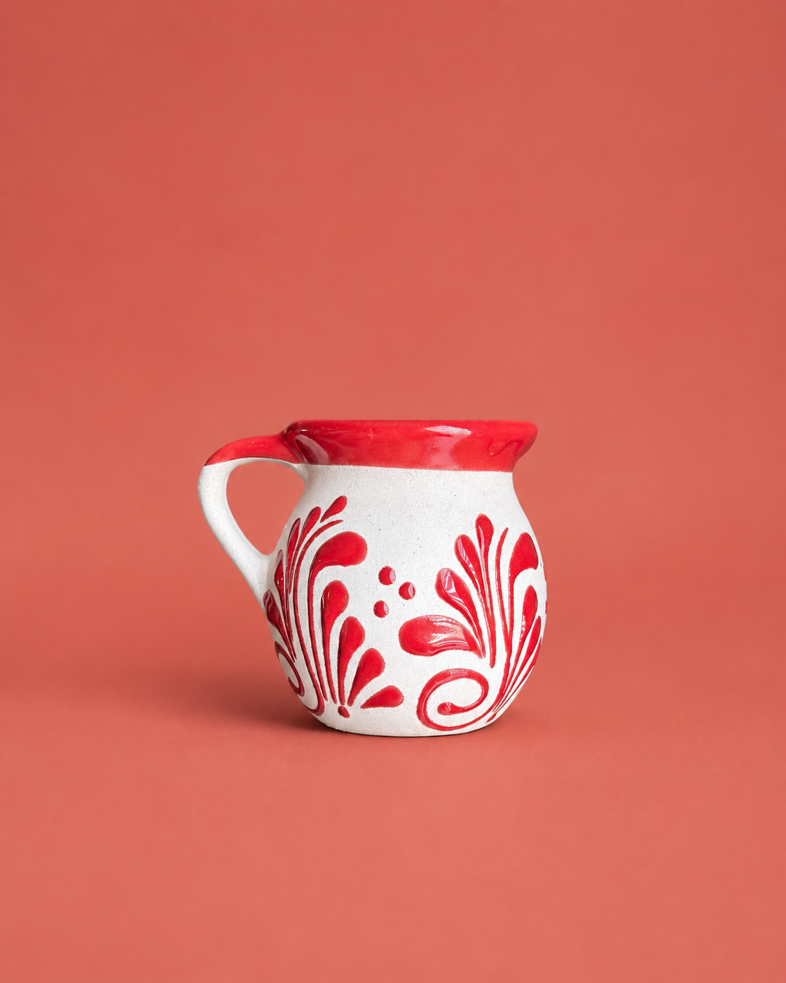 White mug with red floral patterns and rim on a coral background