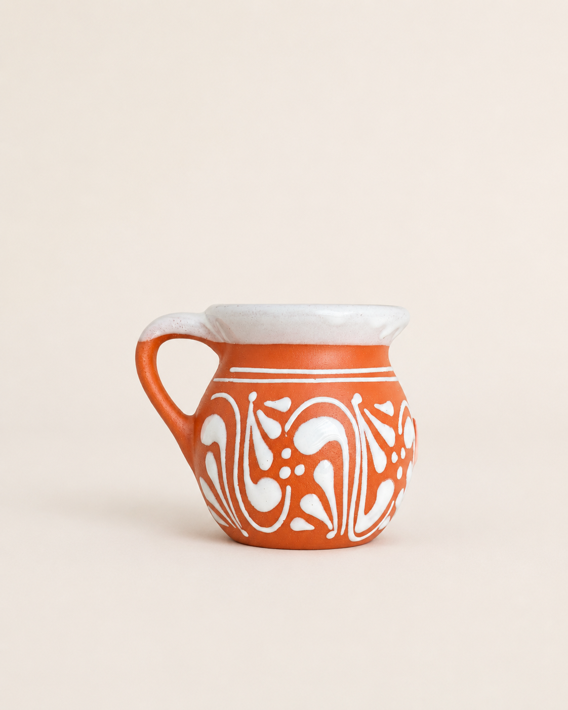 Ceramic pitcher with white handle and decorative patterns on a beige background
