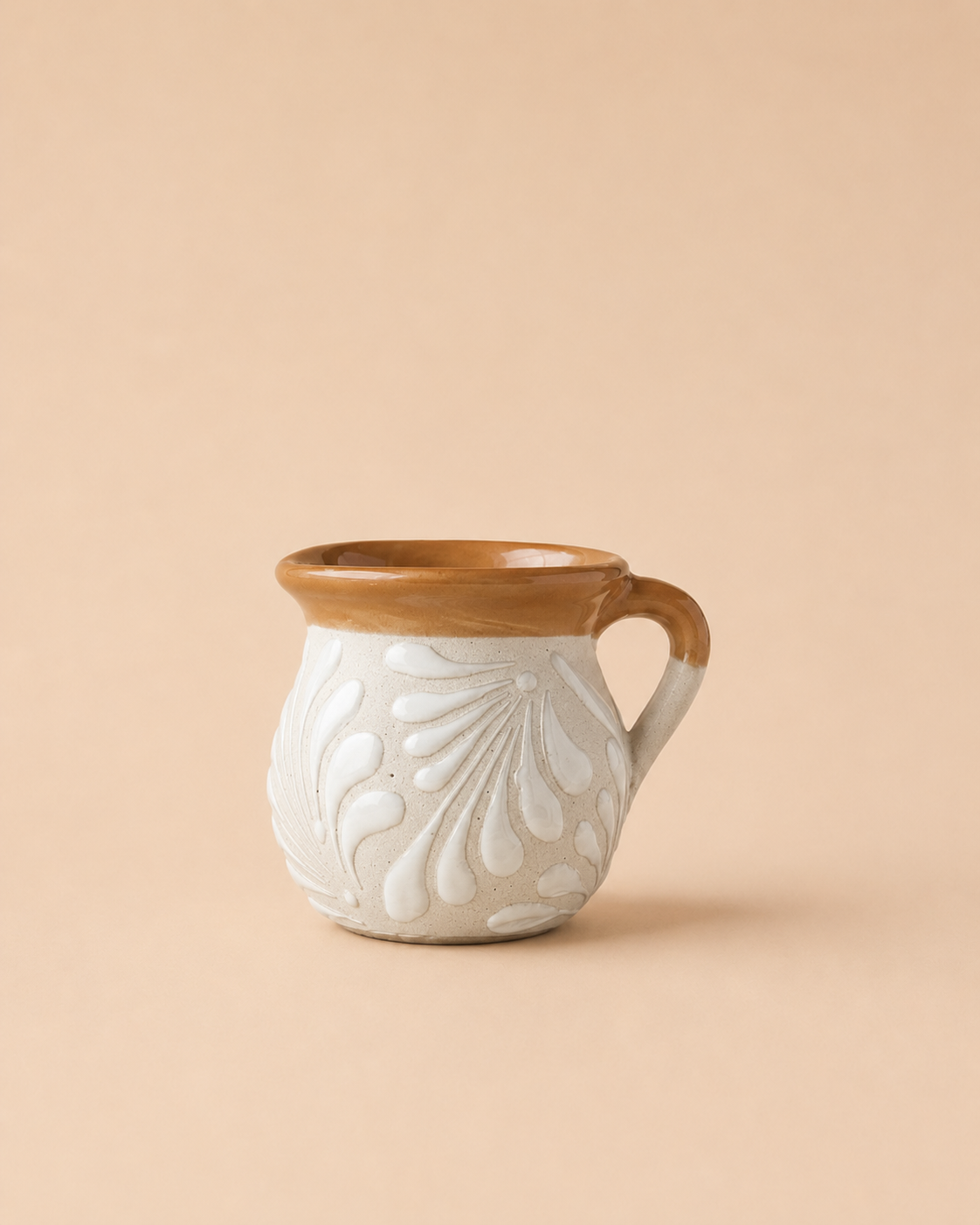 A small ceramic mug with a textured, embossed floral pattern on a warm off-white body, featuring a contrasting glazed brown rim and handle, set against a solid beige background.