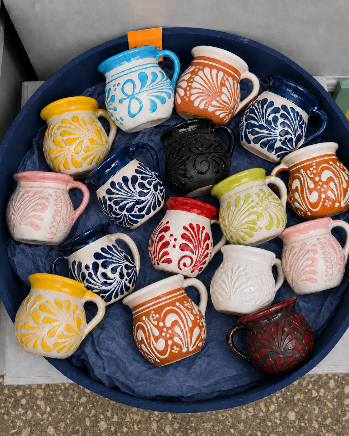 Collection of colorful ceramic mugs with various patterns arranged in a blue tray.