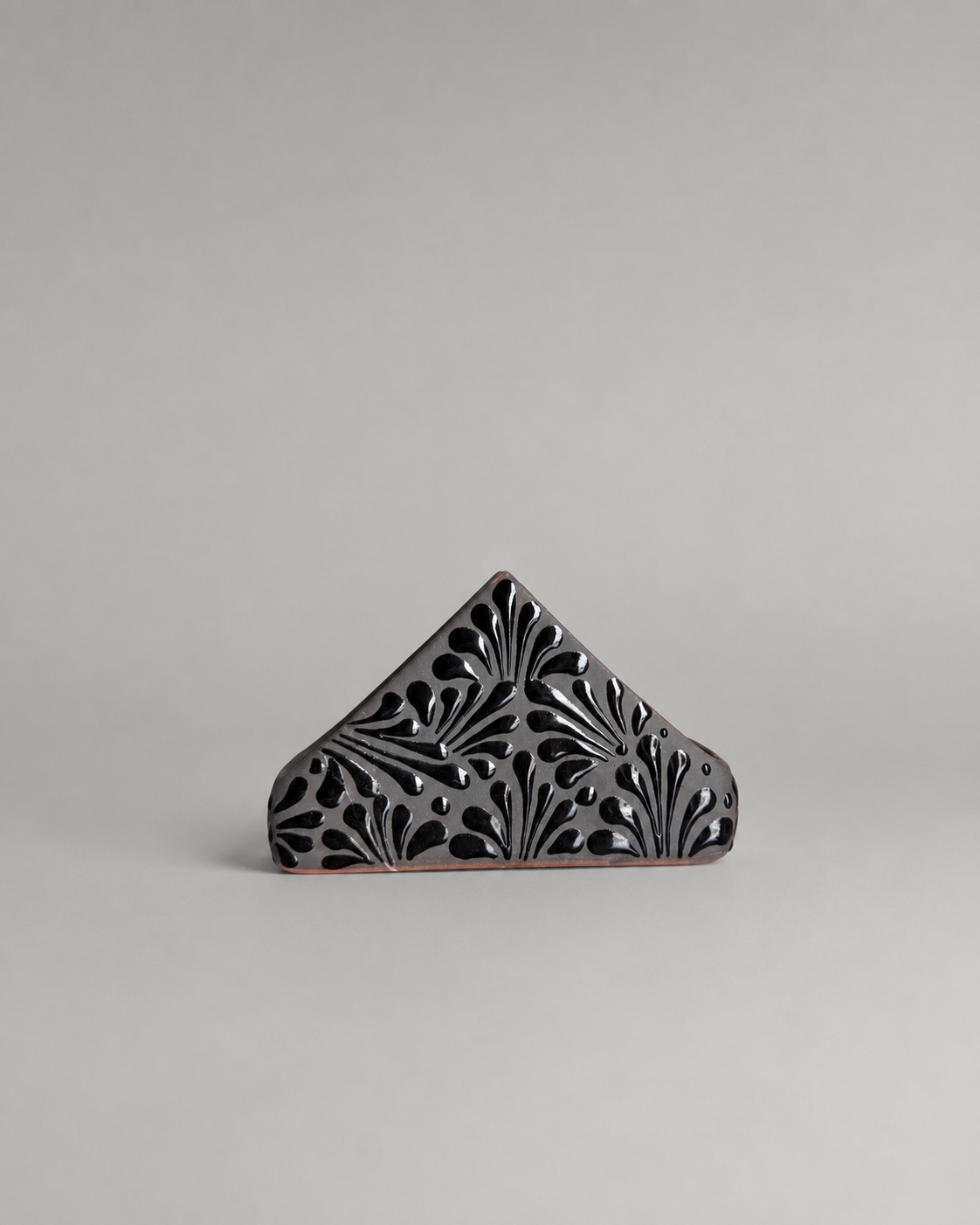 Decorative triangular napkin holder with intricate cut-out patterns on a gray background