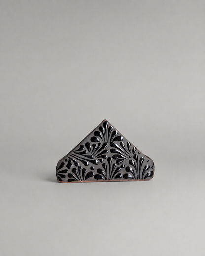 Decorative triangular napkin holder with intricate cut-out patterns on a gray background