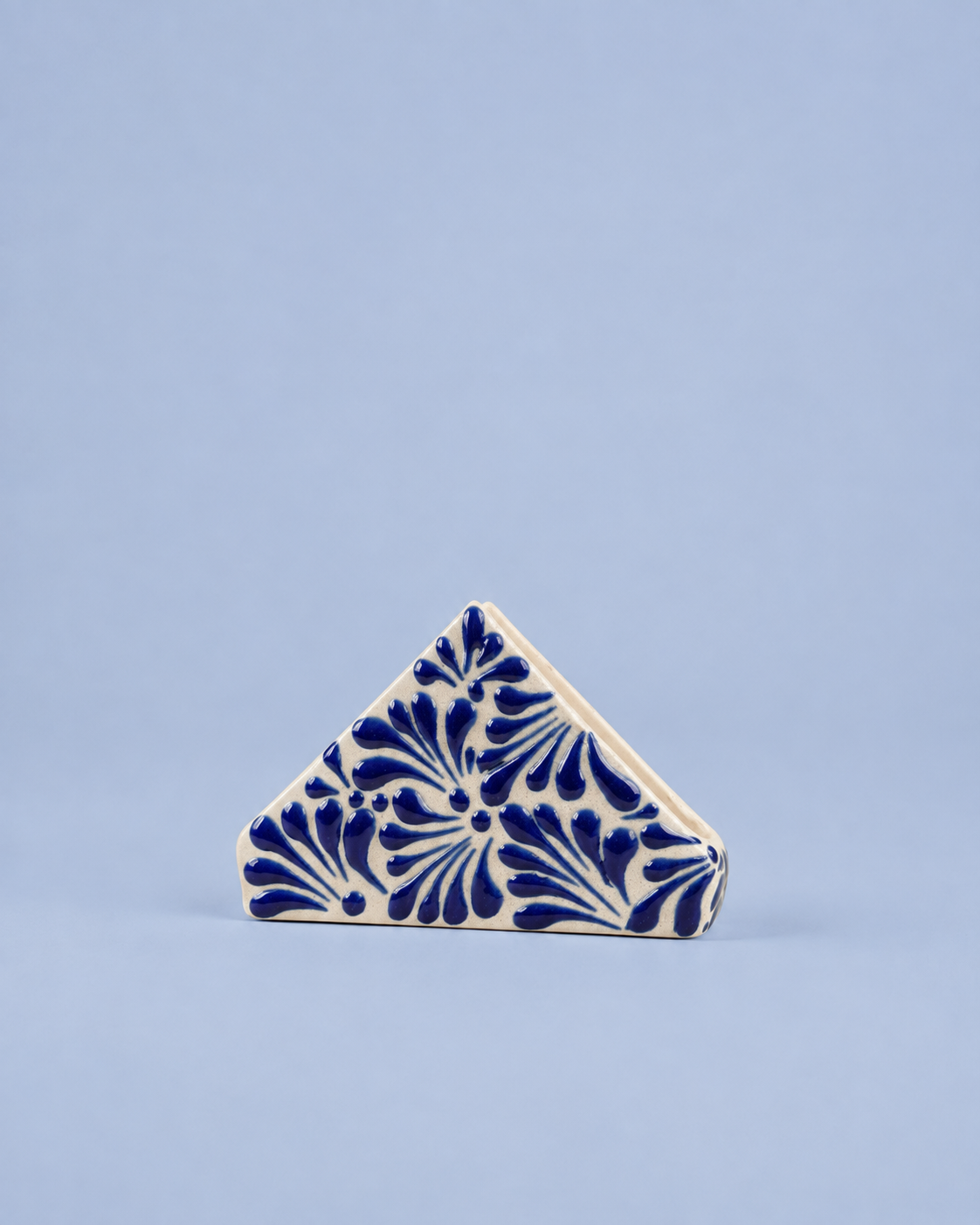 A small triangular ceramic tile with a blue floral pattern on an off-white background, set against a solid light blue backdrop.