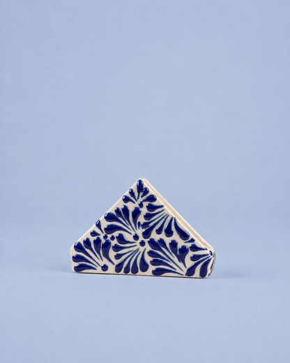 A small triangular ceramic tile with a blue floral pattern on an off-white background, set against a solid light blue backdrop.